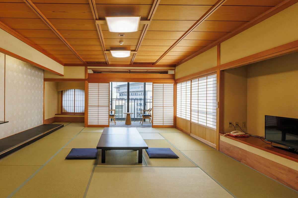 Una habitación japonesa tradicional con suelo de tatami, una mesa baja, puertas correderas y un televisor.