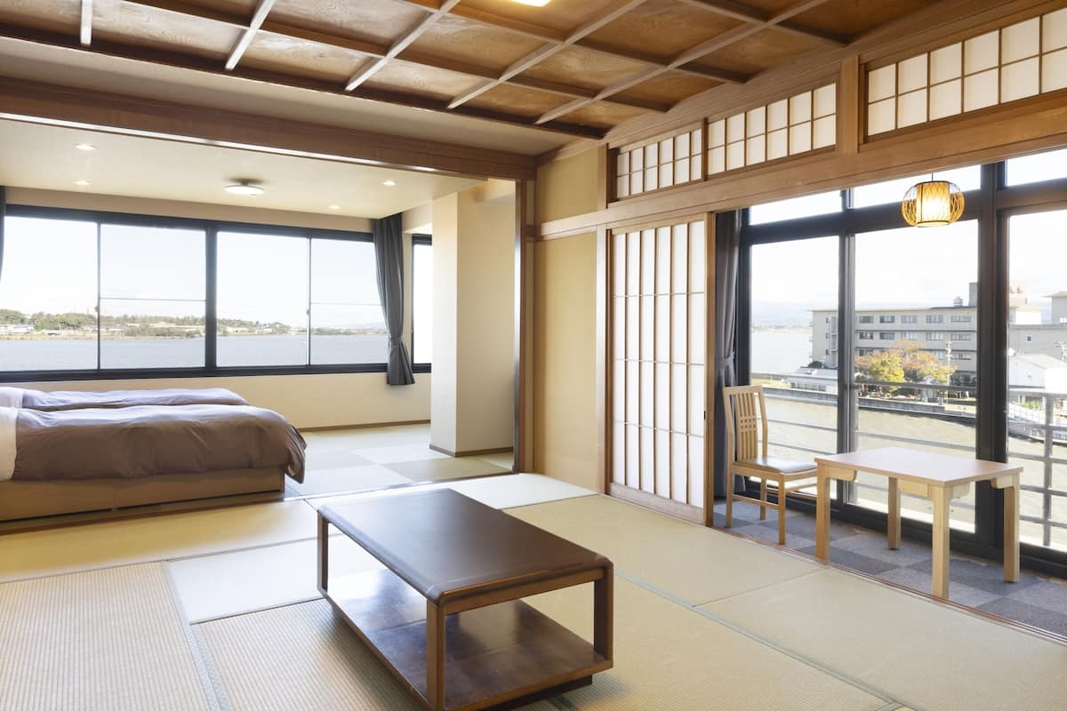 A traditional Japanese-style room with tatami flooring, a bed, a table, and a view of a river.