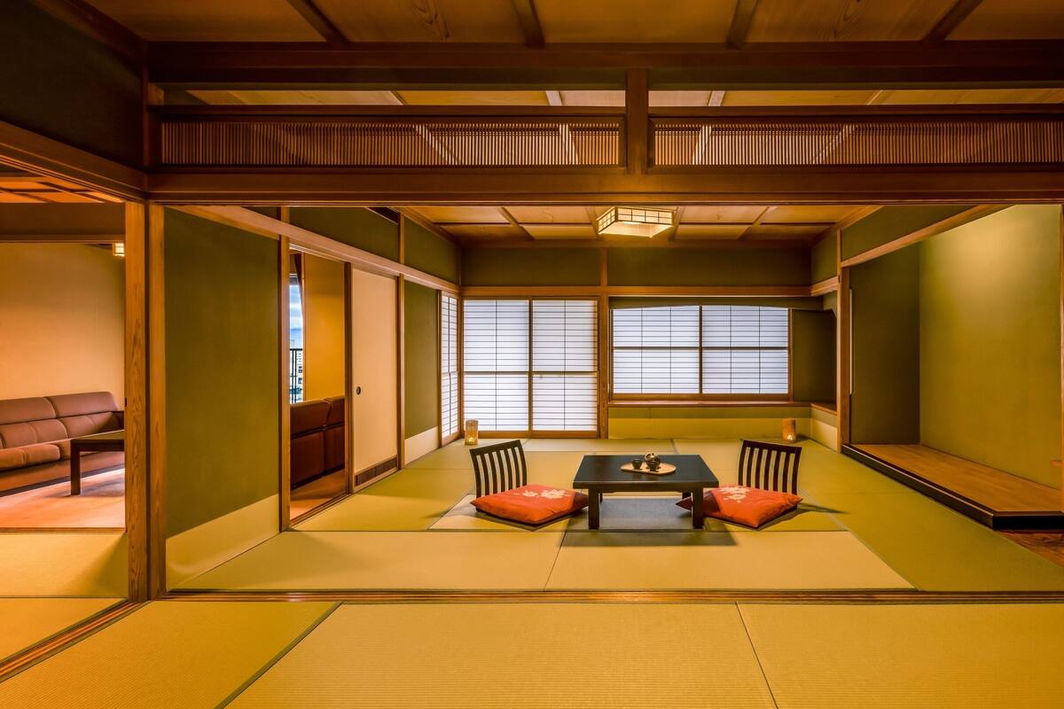 Una habitación japonesa tradicional con suelo de tatami, una mesa baja con cojines, puertas correderas y vistas a través de un shoji.