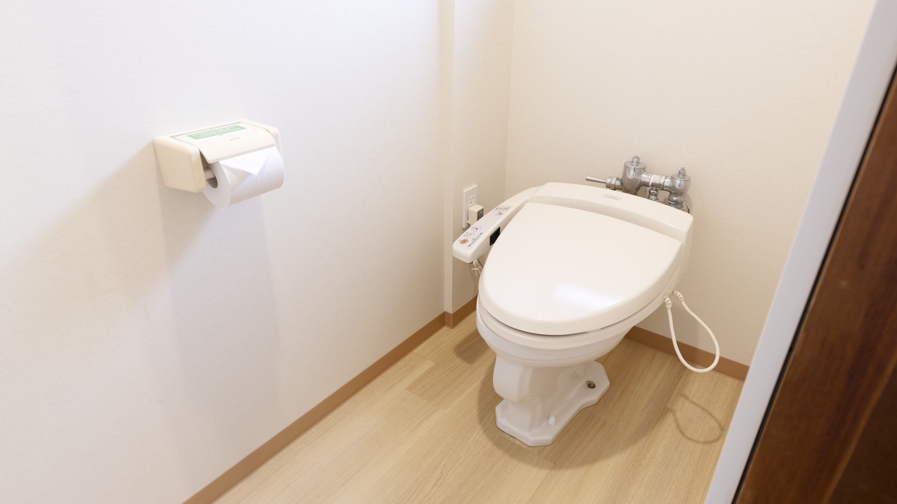 Une petite salle de bain propre, équipée de toilettes, d’un sèche-mains et d’un distributeur de serviettes en papier.