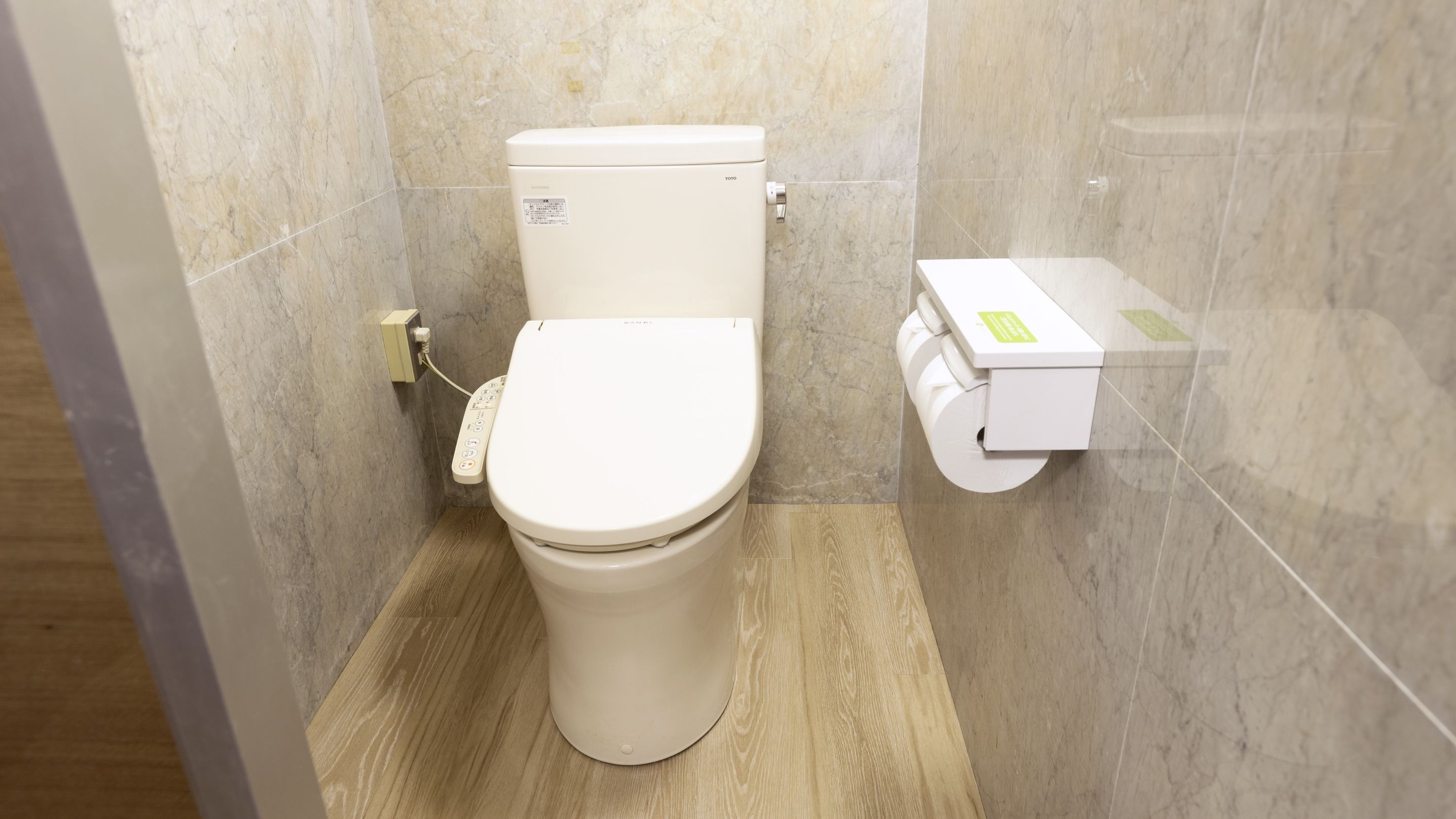 A modern toilet with a control panel, a toilet paper holder, and a marble wall.