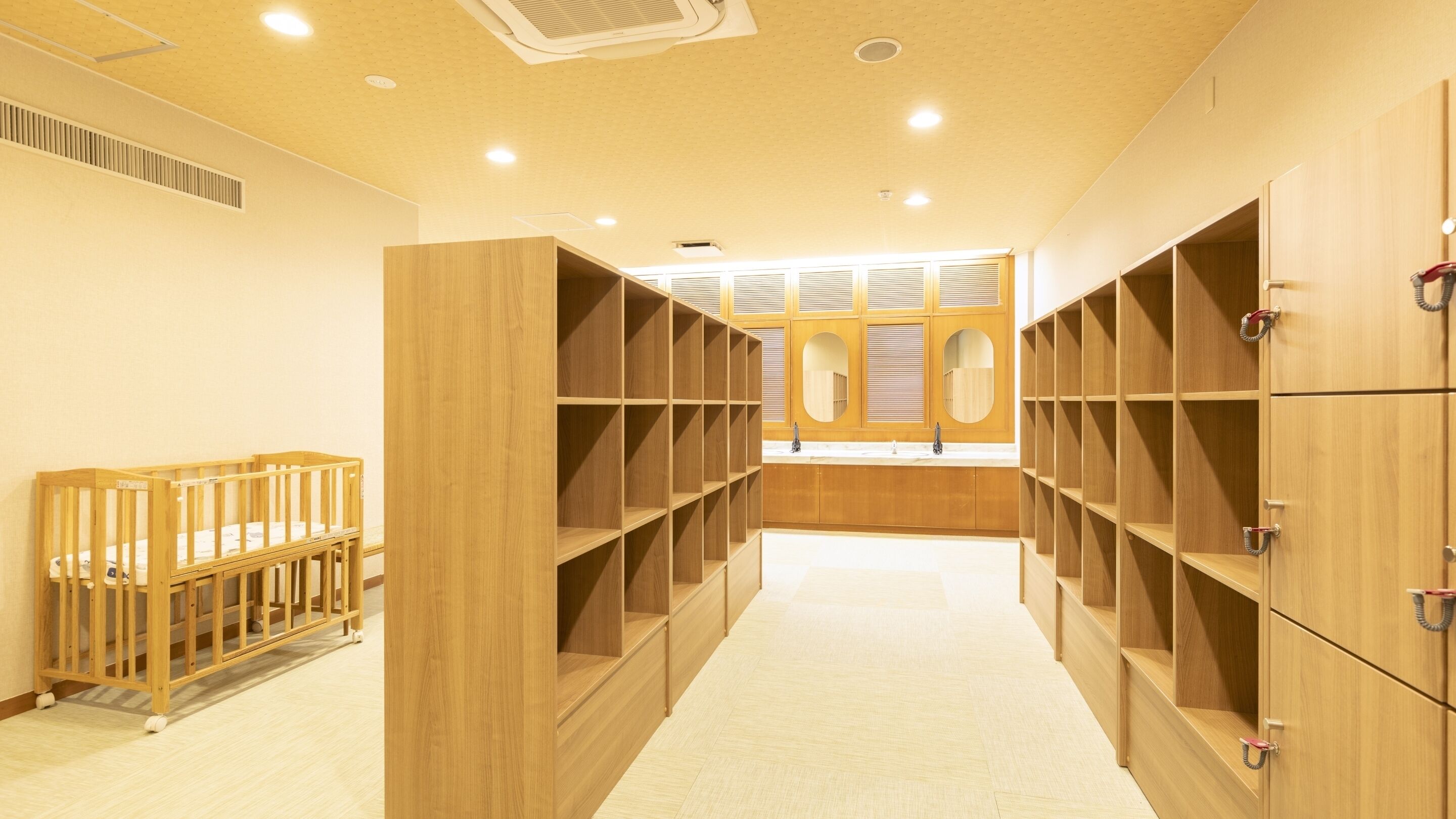 A room with wooden lockers, a baby crib, and a window with blinds.