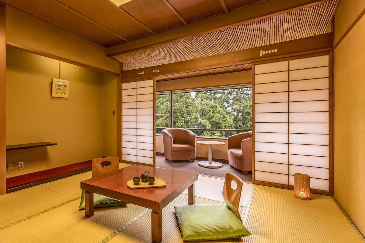 Ein traditioneller japanischer Raum mit Tatami-Bodenbelag, einem niedrigen Tisch mit Kissen und einem verschiebbaren Shoji-Bildschirm.