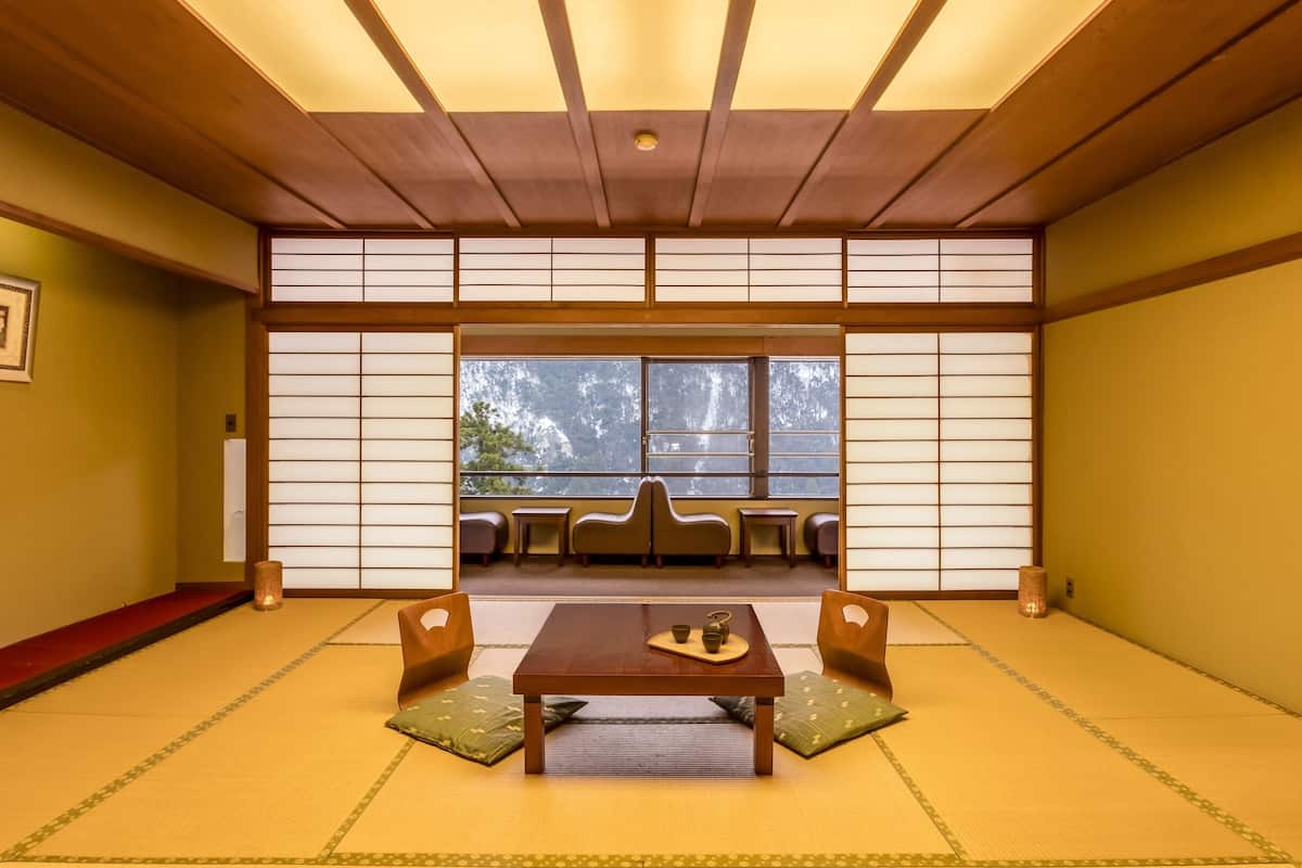 Ein traditioneller japanischer Raum mit Tatami-Boden, einem niedrigen Holztisch, Kissen und verschiebbaren Shoji-Bildschirmen.