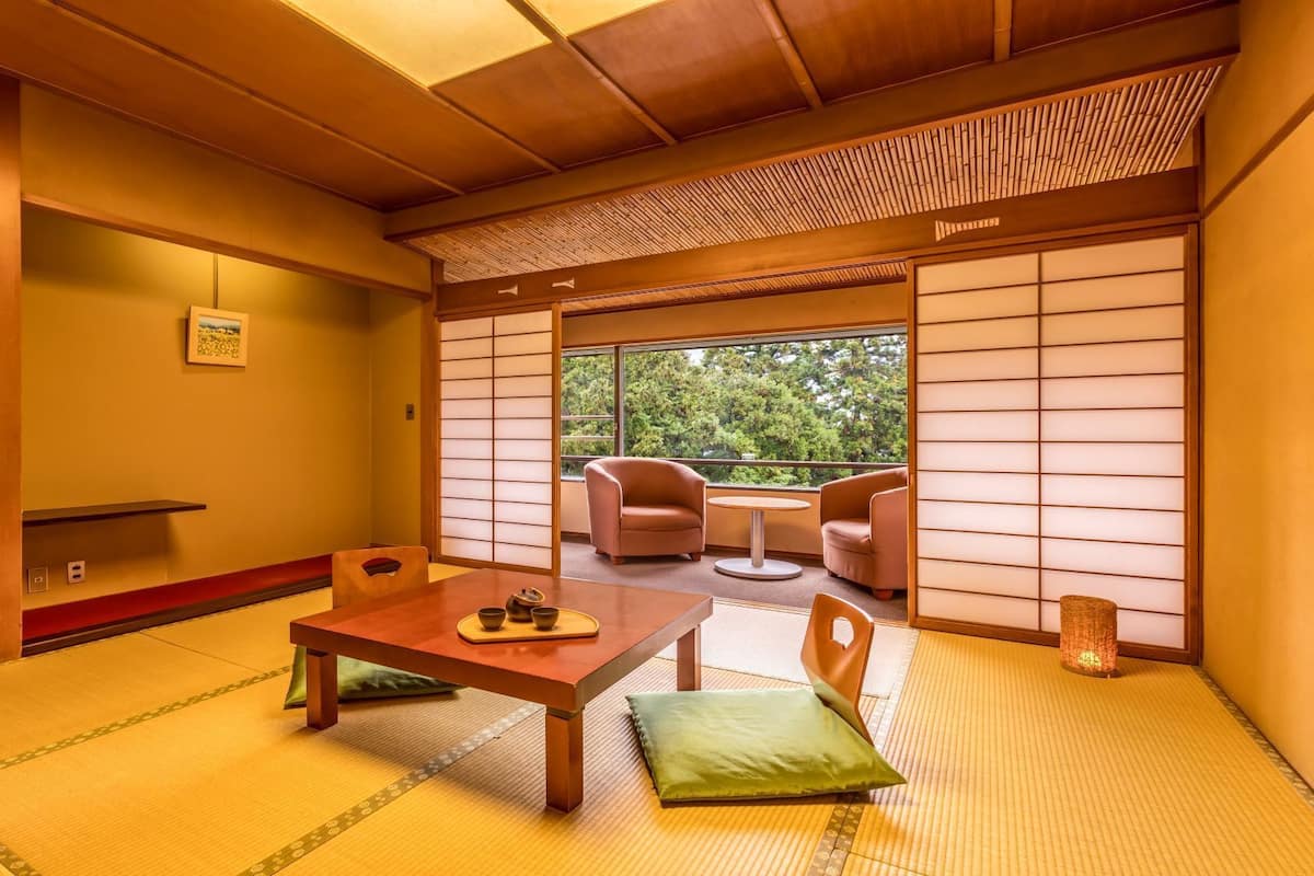 Ein traditioneller japanischer Raum mit Tatami-Boden, einem niedrigen Tisch mit Teeservice und Blick auf Grünfläche.
