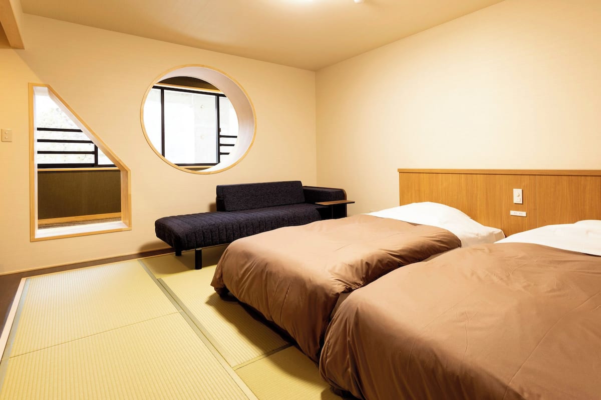 Ein Hotelzimmer mit zwei Betten, einem Sofa, einem kleinen Tisch und einem Fenster mit Blick.