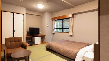 A compact hotel room with a bed, a small desk with a television, a chair, and a table.