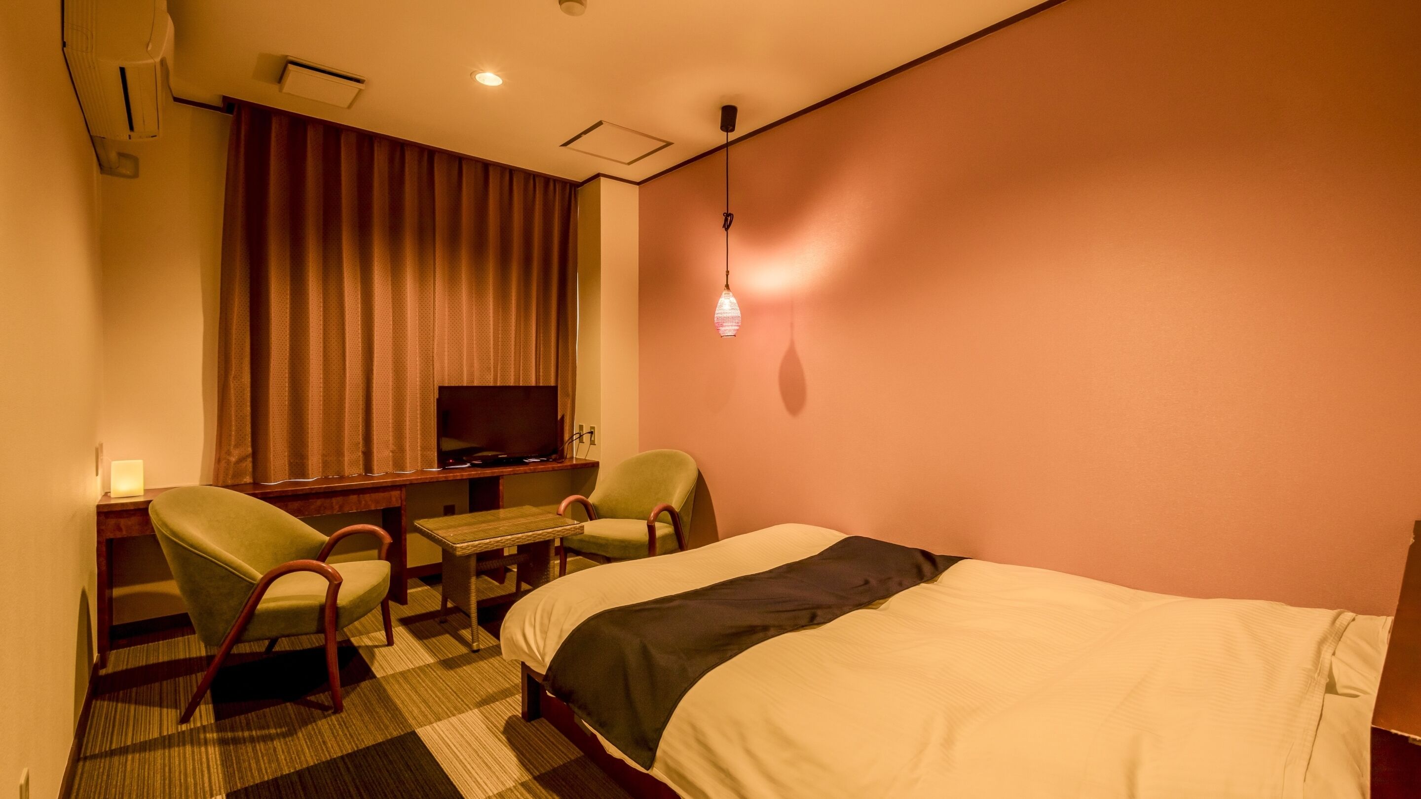 Een hotelkamer met een bed, een bureau, twee stoelen, een televisie en een wandlamp.