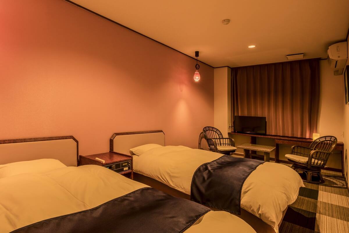 Quarto de hotel com duas camas, televisão, cadeira e uma mesinha.