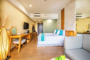 A hotel room with a bed, a sofa, a desk, and a mirror. - Bedrock Hotel (Kuta)
