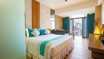 Habitación de hotel con cama, escritorio, silla, vista al exterior y cortinas.