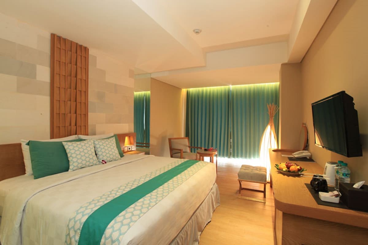 A hotel room with a large bed, a desk with a chair, a television, and a fruit bowl.