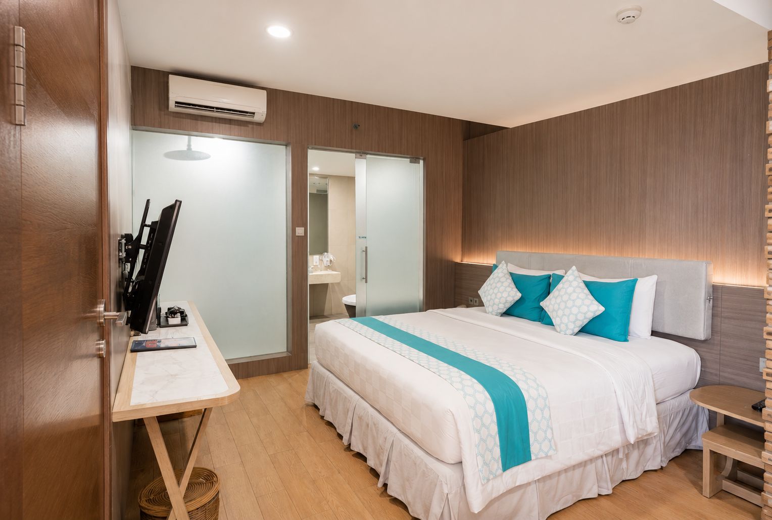 A hotel room with a bed, bedside table, desk, and a mirror.