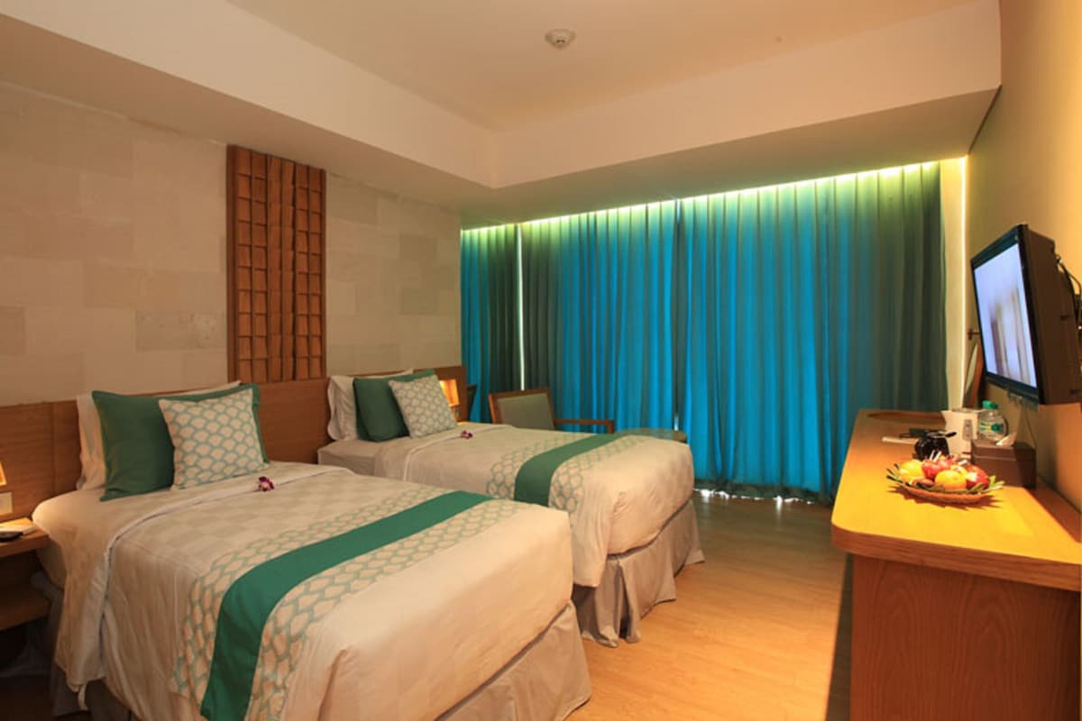 A hotel room with two beds, a desk with a computer, a TV, and a window with blue curtains.