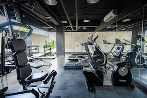 A gym with exercise equipment, including treadmills and a stationary bike, and a weight bench. - Bedrock Hotel (Kuta)