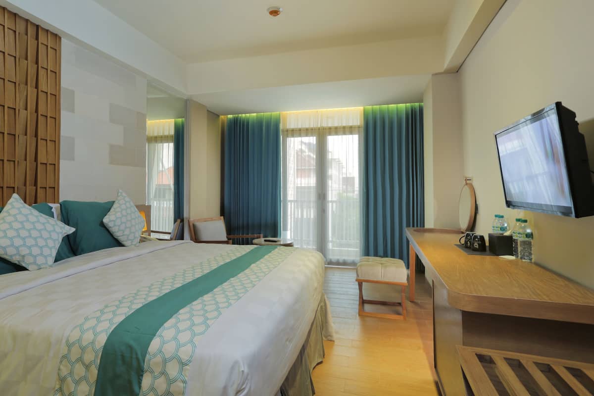Habitación de hotel con una cama grande, un escritorio con silla, televisión y ventana con cortinas.