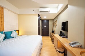 A hotel room with a bed, a desk with a telephone, a television, and a mirror. - Bedrock Hotel (Kuta)