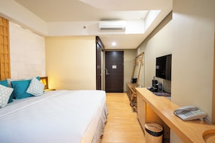 A hotel room with a bed, a desk with a telephone, a television, and a mirror.