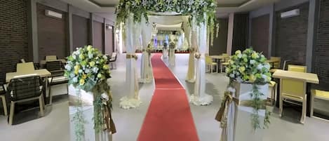A hotel interior with a red carpet aisle, white columns, and floral arrangements.