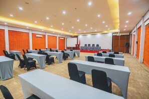 A conference room with multiple tables and chairs, a stage with a podium, and a projector screen. - Bedrock Hotel (Kuta)
