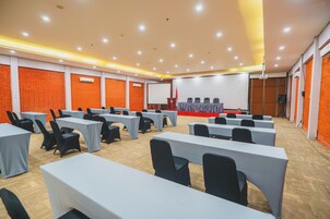 Une salle de conférence équipée de plusieurs tables et chaises, d’une scène avec un pupitre et d’un écran de projection.