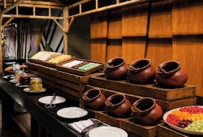 A buffet setup with various food items and traditional pottery. - Bedrock Hotel (Kuta)