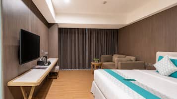Habitación de hotel con cama, escritorio con televisor de pantalla plana, sofá y pequeña mesa con planta.