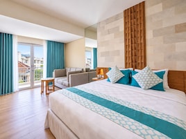 Habitación de hotel con una cama grande, un sofá, una mesita y una mesita de noche con lámpara.