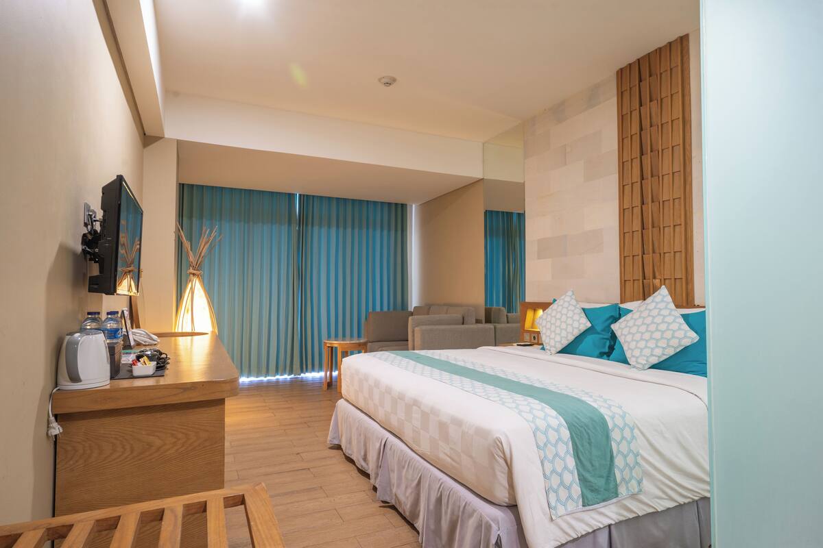 Habitación de hotel con cama, escritorio, silla, televisión y ventana con cortinas.
