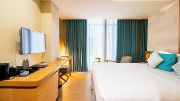 A hotel room with a bed, a desk with a flat-screen TV, a chair, and a window with curtains.