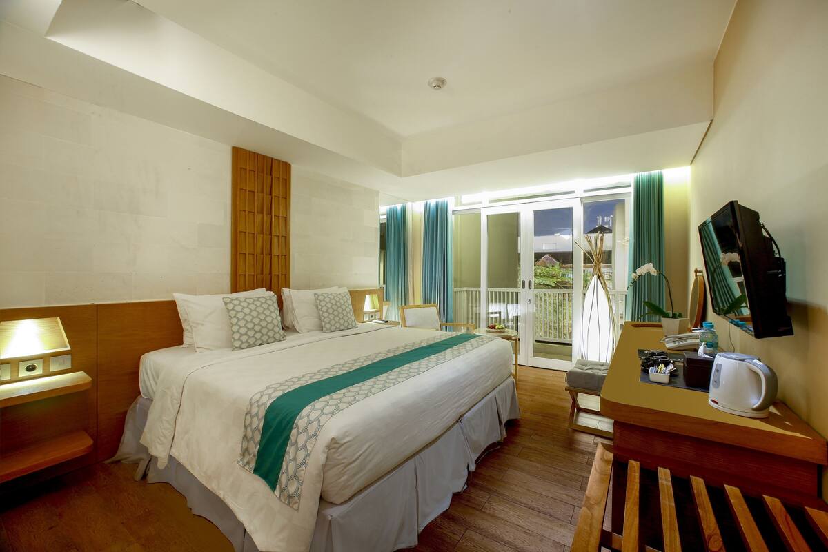 Habitación de hotel con una cama grande, mesitas de noche, un escritorio con hervidor y vistas al exterior.