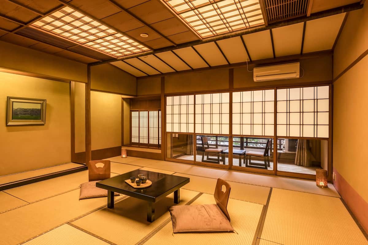 A traditional Japanese room with tatami flooring, a low table with cushions, sliding shoji doors, and a view of the outdoors.