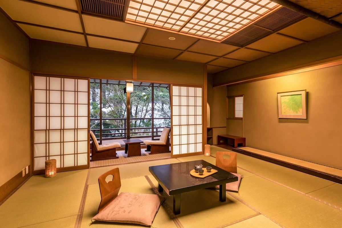 A traditional Japanese room with tatami flooring, a low table with a tea set, and sliding doors with a view of greenery outside.
