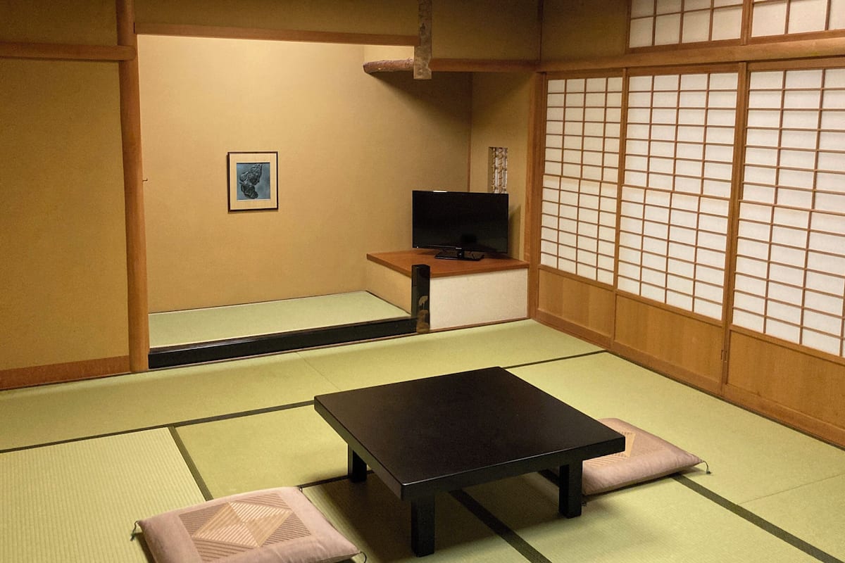 A traditional Japanese room with tatami flooring, a low table, cushions, and a television.
