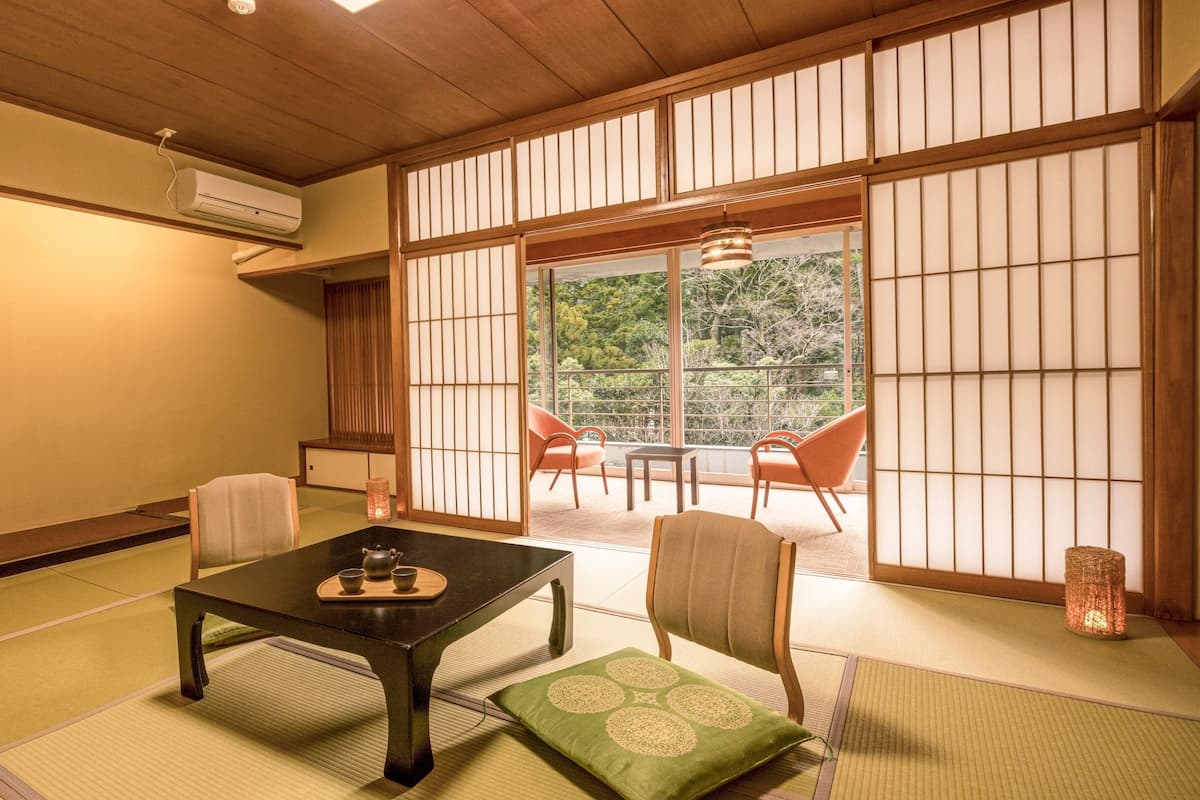A traditional Japanese room with tatami flooring, a low table with a tea set, and sliding shoji doors leading to a balcony with chairs.