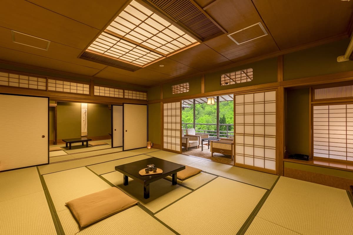 A traditional Japanese room with tatami flooring, sliding doors, and a view of greenery outside.