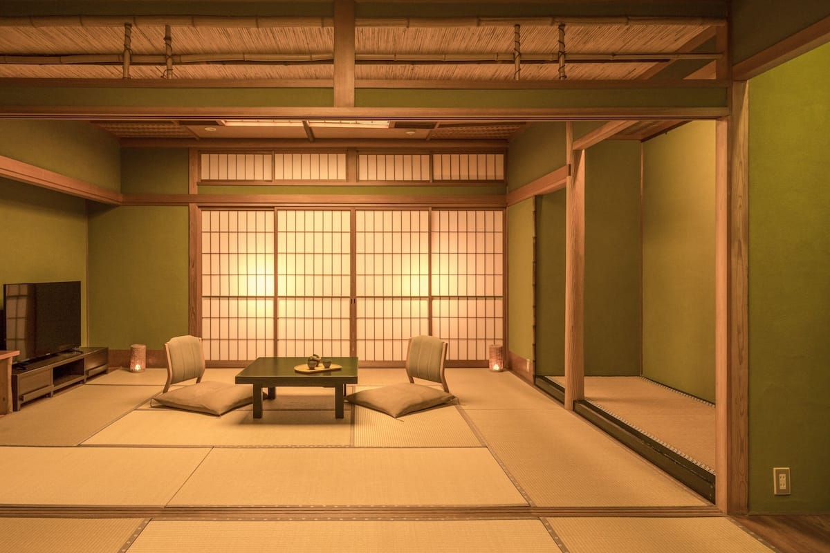 A traditional Japanese room with tatami flooring, a low table with cushions, a television, and sliding shoji doors.