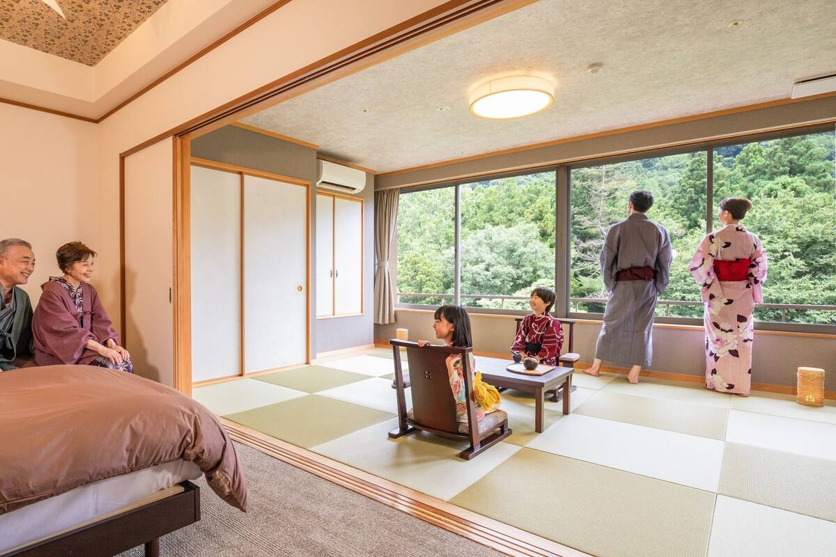 A traditional Japanese room with tatami flooring, a low table, and a large window offering a view of greenery.