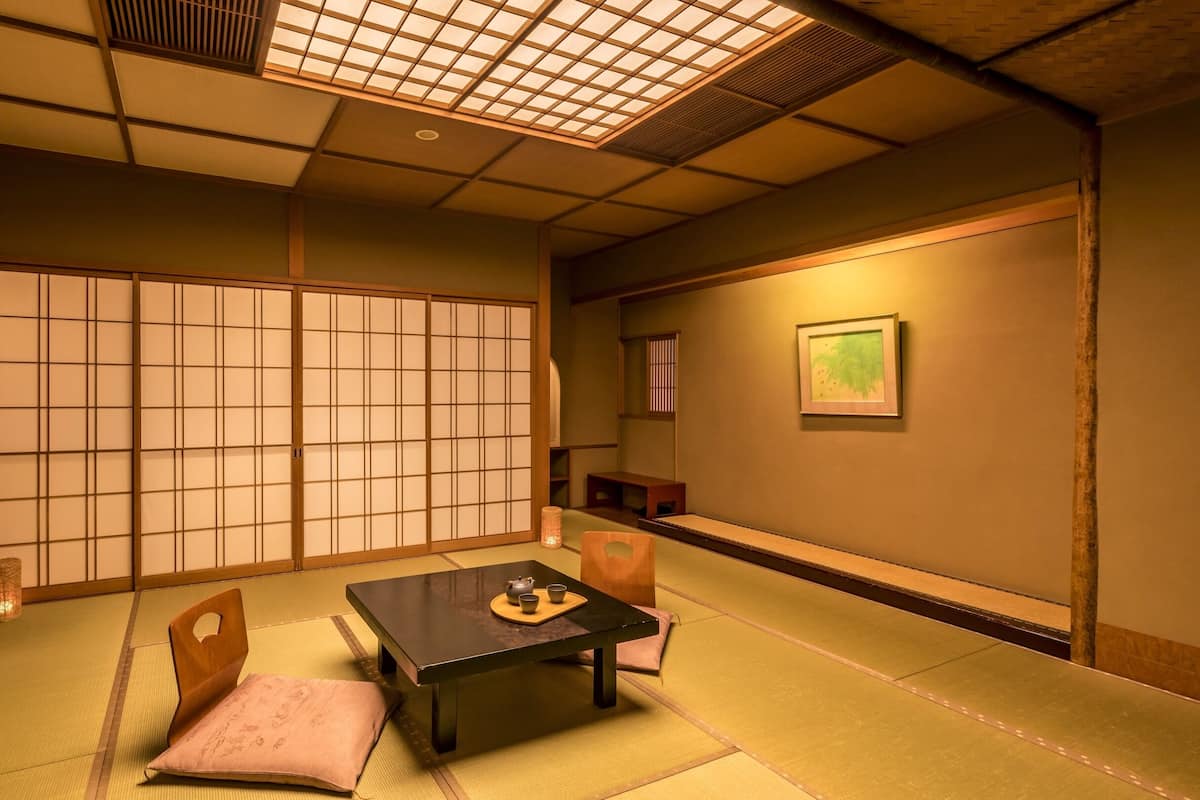 A traditional Japanese room with tatami flooring, a low table with a tea set, sliding doors, and a framed picture on the wall.