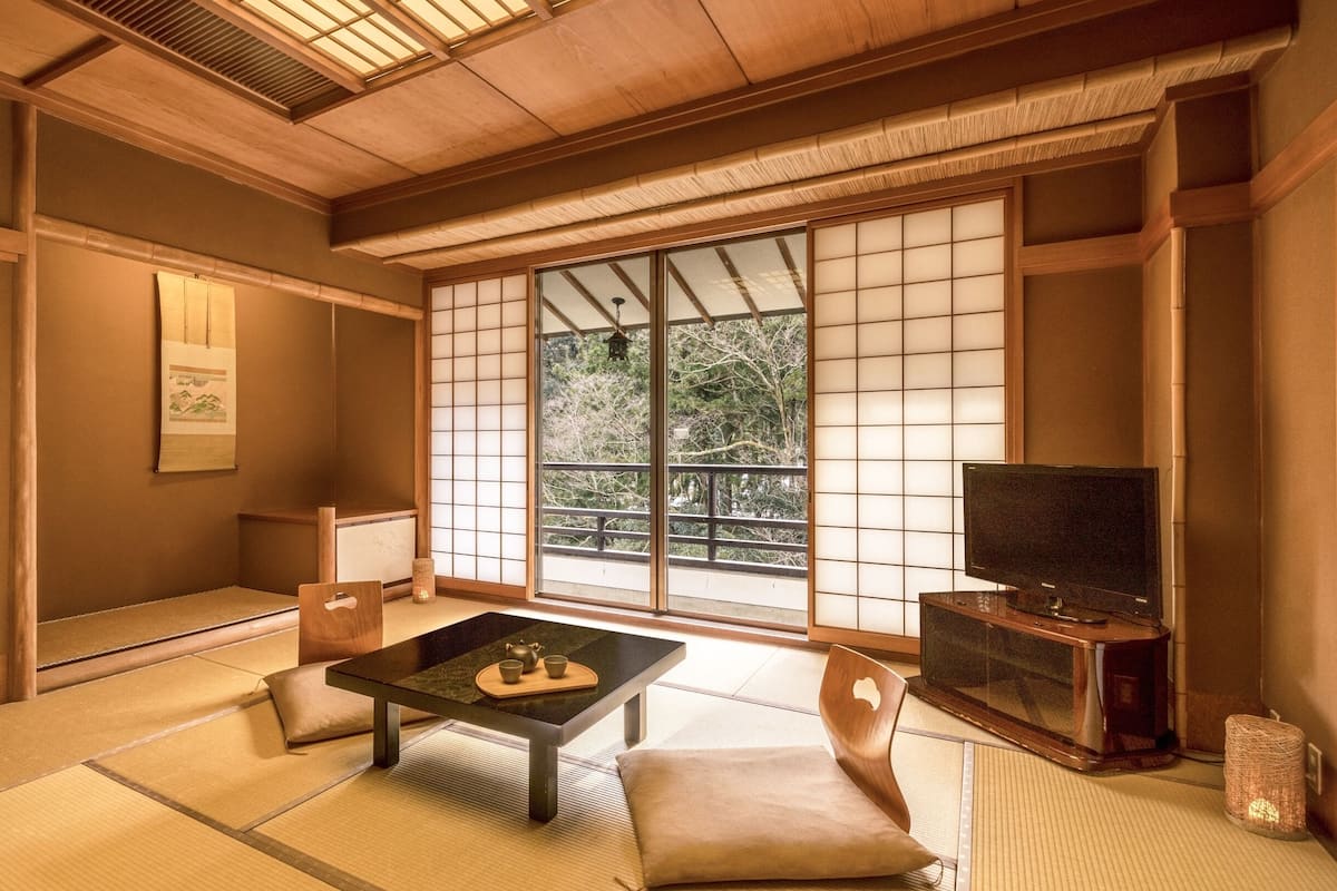 A traditional Japanese room with tatami flooring, a low table with tea set, sliding shoji doors, and a TV on a wooden stand.