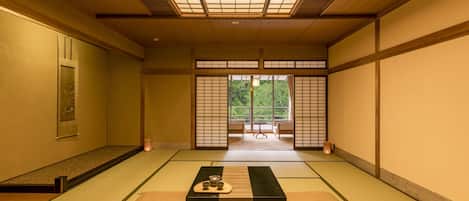 Une pièce de style japonais traditionnel, avec un sol recouvert de tatamis, une petite table sur laquelle est disposé un service à thé, et des portes coulissantes donnant sur un balcon avec vue sur la verdure.