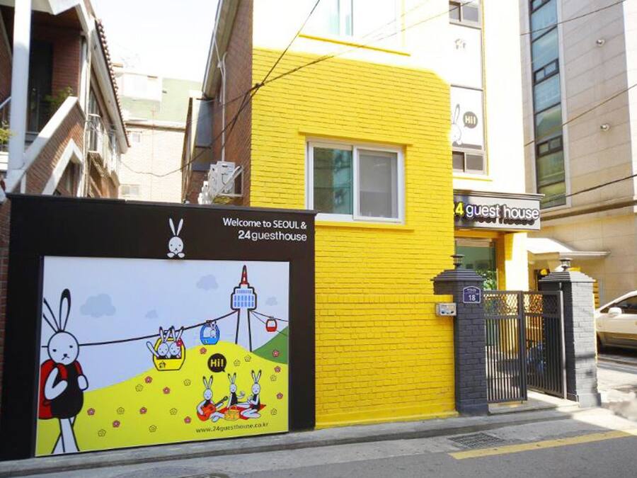 A yellow building with a sign for '4 guest house' and a colorful advertisement for '24 guesthouse' featuring cartoon rabbits and a website URL.