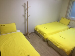 A room with two beds, each with a yellow bedspread and matching pillows, a wooden coat rack, and a window with blinds. - 24 Guesthouse Seoul Cheongryangri (Seoul)