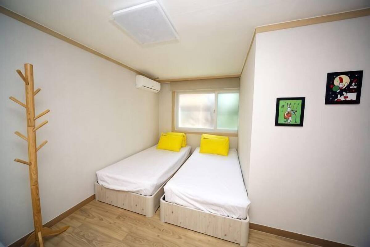 Een kleine, lichte kamer met twee eenpersoonsbedden, een raam en een kapstok.