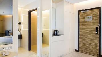 Une chambre d’hôtel moderne équipée d’un lit, d’un bureau avec un téléphone, d’un espace douche et d’une porte en bois avec une pancarte.