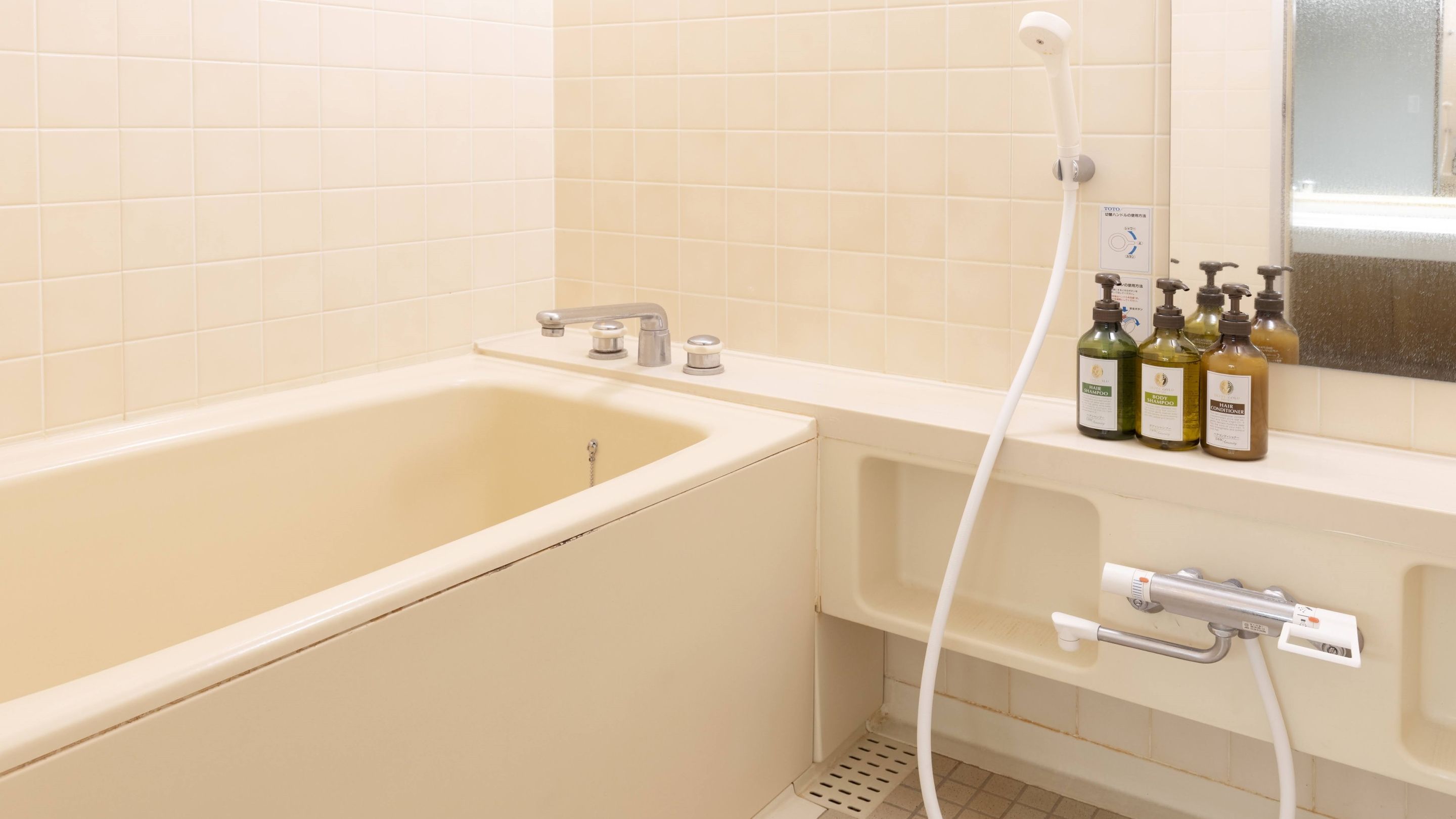 Une salle de bain avec une baignoire, une douche et un lavabo. On peut voir des bouteilles de shampoing et d’après-shampoing sur le lavabo.