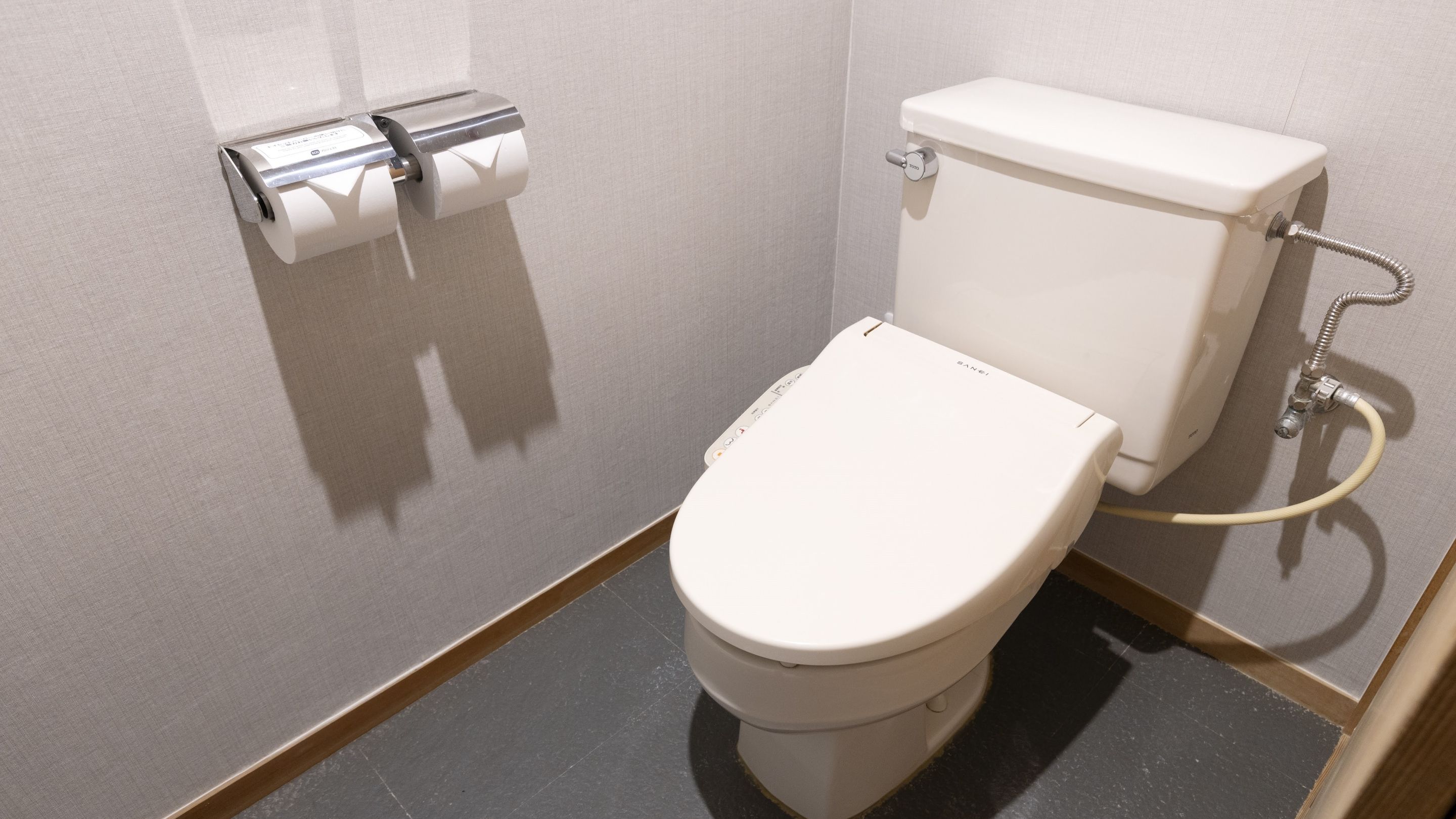 Des toilettes classiques, dotées d’une chasse d’eau à levier, d’un porte-rouleau de papier toilette et d’un accessoire de type bidet.