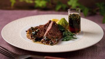 A plate with a steak and a glass of beverage on a textured tablecloth.