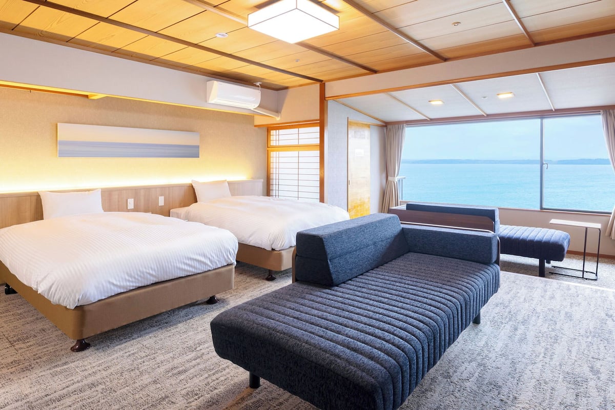 Une chambre d’hôtel avec deux lits, un canapé, une petite table et une grande fenêtre donnant sur la mer.