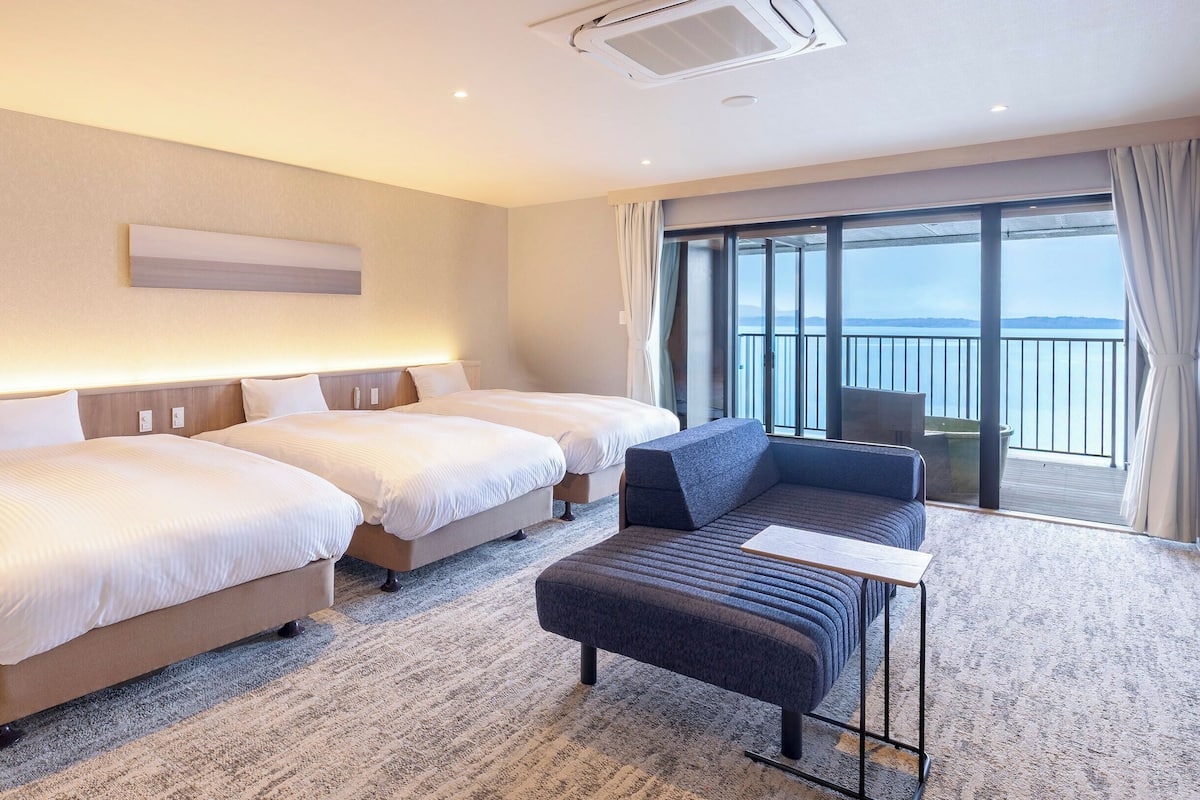 Une chambre d’hôtel avec deux lits, un canapé, une petite table et une grande fenêtre donnant sur la mer.